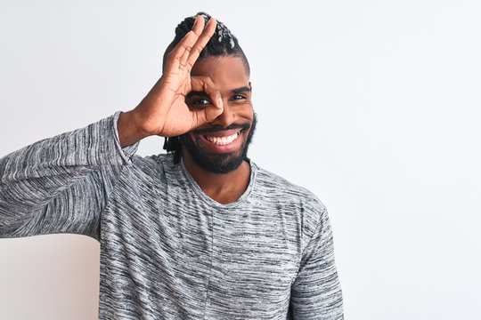 African american man with braids wearing grey sweater over isolated white background doing ok gesture with hand smiling, eye looking through fingers with happy face.