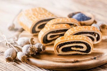 Poppy roll cake on wooden rustic table. Traditional christmas strudel with poppies heads and seed in background.