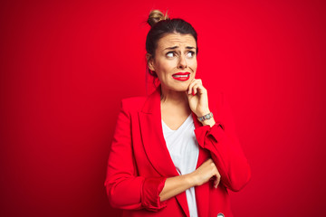 Young beautiful business woman standing over red isolated background Thinking worried about a question, concerned and nervous with hand on chin