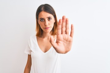 Beautiful redhead woman wearing casual white t-shirt over isolated background doing stop sing with palm of the hand. Warning expression with negative and serious gesture on the face.