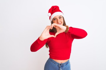 Young beautiful girl wearing Christmas Santa hat standing over isolated white background smiling in love doing heart symbol shape with hands. Romantic concept.