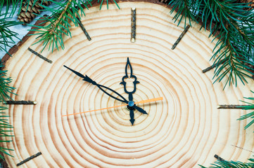 Christmas wooden clock shows the time ten to twelve at night on the edge of the clock green spruce branches and cones top view