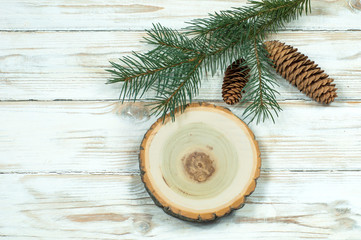 Fototapeta na wymiar fir branches with cones and a wooden disk on a white wooden background top view
