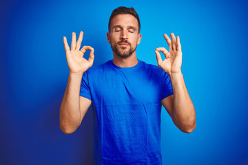 Young handsome man wearing casual t-shirt over blue isolated background relax and smiling with eyes closed doing meditation gesture with fingers. Yoga concept.