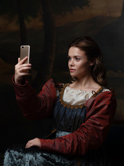 Old and new, concept. Beautiful young Renaissance style woman taking selfie on phone.