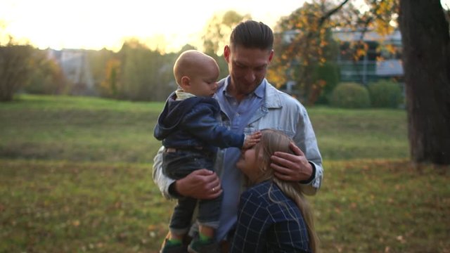 Young attractive father walks in the park with two children. A man holds a little son in his arms and hugs the daughter teenager. Fathers day