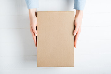 Rectangular cardboard box in female hands. Top view, white background - obrazy, fototapety, plakaty