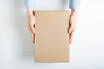 Rectangular cardboard box in female hands. Top view, white background