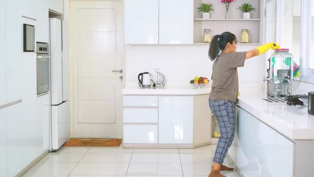 Happy young woman dancing and cleaning kitchen using a feather duster. Shot in 4k resolution