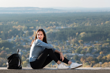 Young beautiful girl sits on a hill. Forest in the distance. sunny day