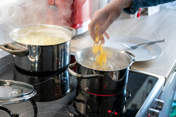 Hausfrau kocht Nudeln und Wasser für das Mittagessen mit der Familie in silbernen Töpfen auf Induktionsherd mit heißen Kochfeldern als leckeres Mahl