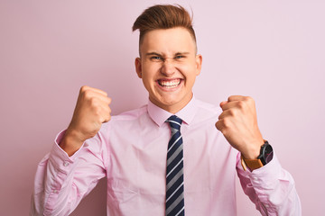 Young handsome businessman wearing shirt and tie standing over isolated pink background angry and mad raising fists frustrated and furious while shouting with anger. Rage and aggressive concept.