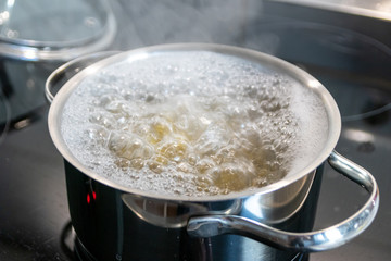 Mittagessen im dampfenden Kochtopf wird auf heißer Herdplatte in der Küche von einer Hausfrau...