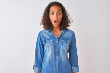 Young brazilian woman wearing denim shirt standing over isolated white background afraid and shocked with surprise and amazed expression, fear and excited face.