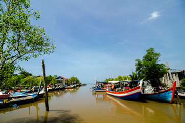 Beautiful rural scenery, fisherman boat moored near wooden jetty over blue sky background