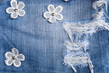 Denim Fabric pattern blue Jeans old ripped torn vintage fashion design decoration by white flowers and buttons background  Jean texture closeup soft focus.