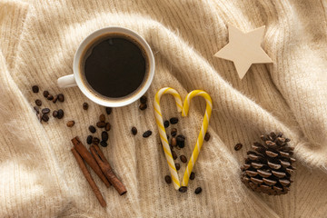 Obraz na płótnie Canvas Top view of Coffee cup, Christmas candies, pine cone, cinnamon sticks, coffee beans on a warm knit wool plaid.
