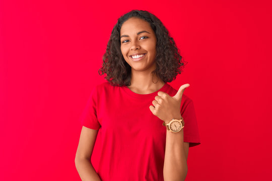 Young brazilian woman wearing t-shirt standing over isolated red background happy with big smile doing ok sign, thumb up with fingers, excellent sign