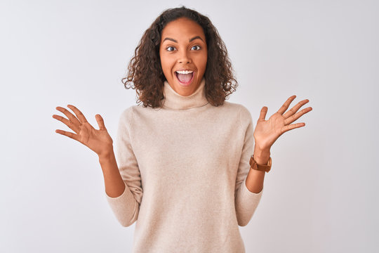 Young brazilian woman wearing turtleneck sweater standing over isolated white background celebrating crazy and amazed for success with arms raised and open eyes screaming excited. Winner concept