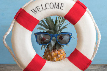 Pineapple in sunglasses and lifebuoy on a blue background. Summer, marine, beach concept.