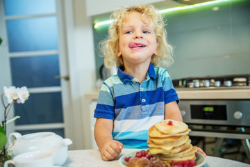 Little curly boy eating sweet pancakes