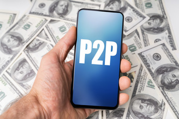 Hand Holding Mobile Phone With P2p Text Against Dollar Bills