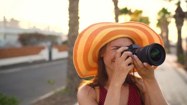 Photographer tourist woman in a big yellow hat taking photos with camera in a beautiful tropical landscape at sunset