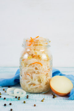 Fermented cabbage in a jar stands in the center on a wooden table. Vertical orientation.