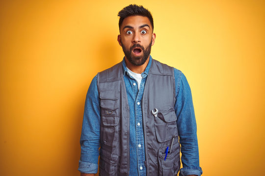 Handsome indian technician man wearing uniform over isolated yellow background afraid and shocked with surprise expression, fear and excited face.