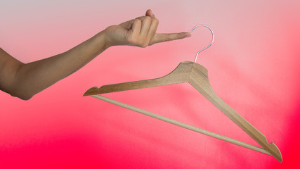 Wooden clothes hanger hanging from a female finger on a red background. Getting ready for shopping. Sale at the clothing boutique.