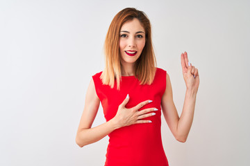 Redhead businesswoman wearing elegant red dress standing over isolated white background smiling swearing with hand on chest and fingers up, making a loyalty promise oath