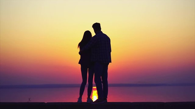 The man and woman walk and hug against the beautiful sunset
