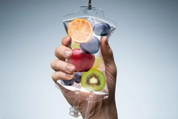 Fotobehang Human Hand Holding Saline Bag With Fruit Slices Over Grey Background © Andrey Popov