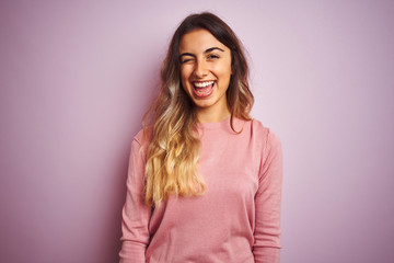 Young beautiful woman wearing a sweater over pink isolated background winking looking at the camera...