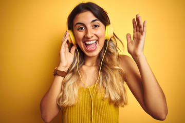 Young beautiful woman wearing headphones over yellow isolated background very happy and excited, winner expression celebrating victory screaming with big smile and raised hands