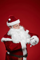 Santa Claus in red costume standing and looking at watch he checking his time isolated on red background
