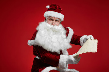 Portrait of Santa Claus looking at camera while sitting and reading Christmas letter in his hands from children