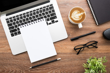 Wood office desk table with blank notebook, laptop computer, cup of latte coffee and supplies. Top...