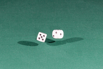 Two white dices falling on a green table