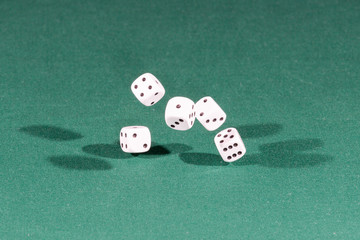 Five white dices falling on a green table