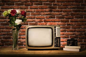 Retro old TV with vintage camera on wooden table in room, brick wall background, vintage filter style