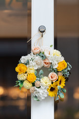 Round front door wreath with yellow and green small flowers on the wooden glass doors with reflection
