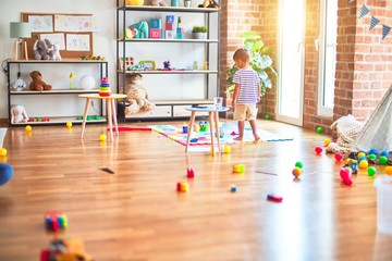 Obraz premium Beautiful toddler boy standing at kindergarten with lots of toys