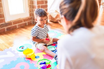 Beautiful toddler boy sitting on puzzle playing with plastic plates, fruits and vegetables at kindergarten
