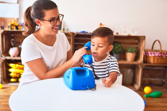 Beautiful teacher and toddler boy playing with vintage blue phone at kindergarten