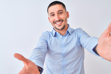 Young handsome business man standing over isolated background looking at the camera smiling with open arms for hug. Cheerful expression embracing happiness.