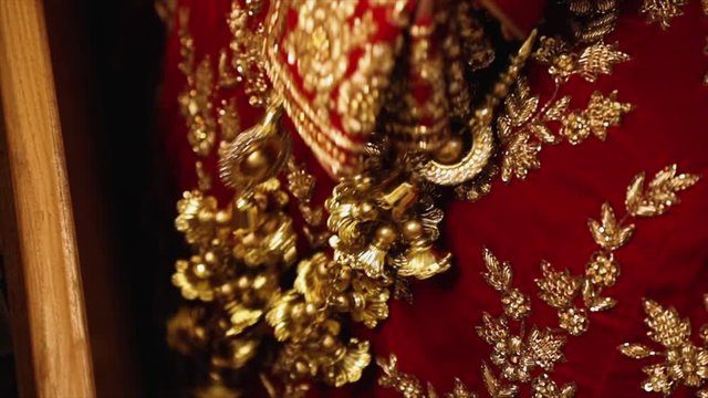 Bell-like shape gold ornaments attached to the bride's dress during an Indian wedding, slow motion shot.