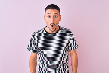 Young handsome man wearing striped t-shirt standing over pink isolated background afraid and shocked with surprise expression, fear and excited face.