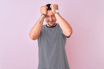 Young handsome man wearing striped t-shirt standing over pink isolated background suffering from headache desperate and stressed because pain and migraine. Hands on head.