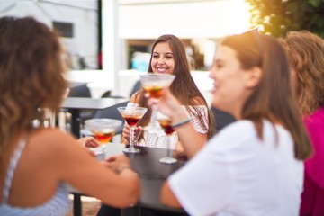 Beautiful group of women sitting at terrace of restaurant drinking cocktails speaking and smiling
